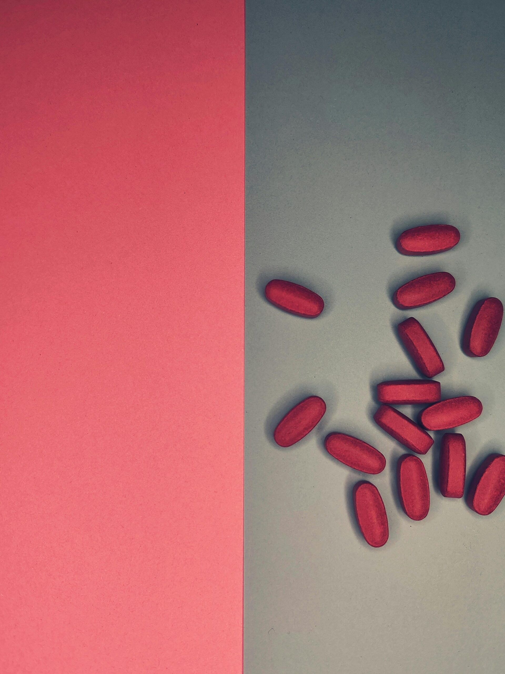 Artistic still life featuring red pills on a red and grey background.